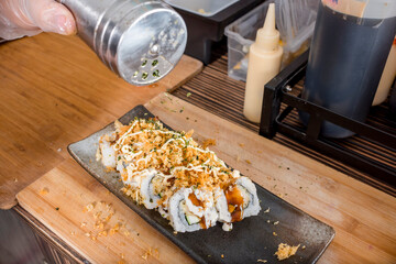 Sprinkling Furikake on top of a Tempura Maki. Final garnish step in preparing sushi rolls.