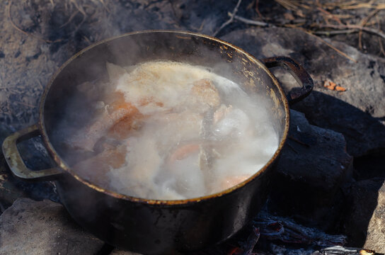 Cooking traditional uha on the campfire. Cast-iron cauldron with