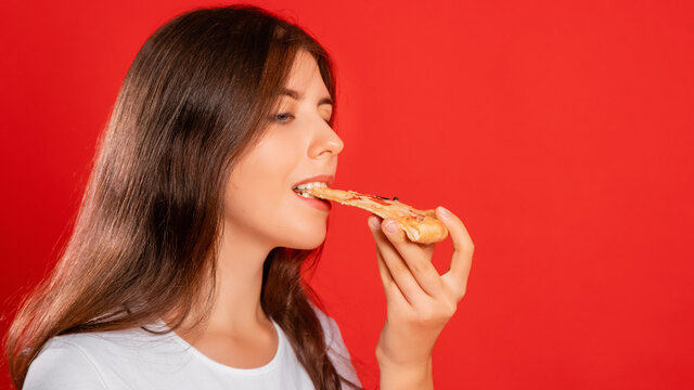 Close up portrait of a young woman in a white t-shirt eating a slice of pizza isolated on a red background. Copy space for label, mockup.