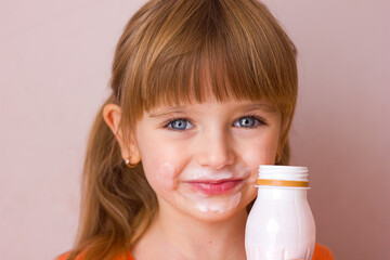 Portrait of a little beautiful girl with emotions on her face, her mouth stained with milk, holding a plastic bottle with a milk drink, yogurt or kefir, selective focus	