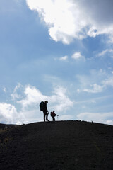 Silhouette portrait photo of two people climbing a mountain against a sky background