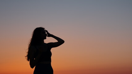 Silhouette of female athlete with slender body resting after evening exercises on beach. Amazing...