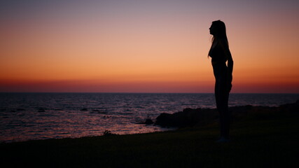 Fototapeta premium Fitness woman in silhouette doing squats exercises on beach near ocean. Young female in sportswear spending evening time for outdoors activity. Amazing colorful sunset on background.