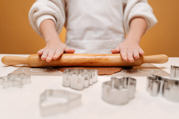 Obraz premium A woman rolls gingerbread dough for Christmas cookies on a white table with a wooden rolling pin.