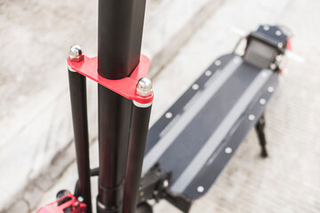 The handlebar stem of an electric scooter parked by the edge of a concrete paved road.
