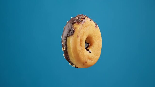 Chocolate donut rotating at blue background. Bakery and food concept. Delicious donut. Flying sweet dessert in 4K, UHD