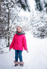 Little girl in a bright jacket plays in the winter forest