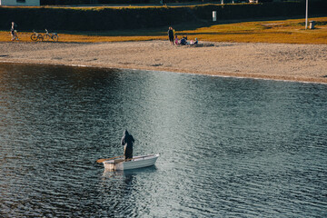 Człowiek łowiący ryby z łódki na jeziorze przy brzegu - obrazy, fototapety, plakaty