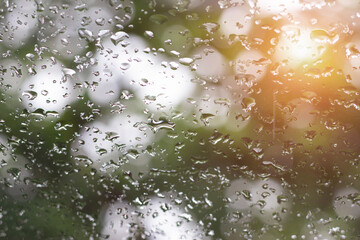 Water droplets on car windshield due to downpour with gray blurred background White bokeh and orange sunlight