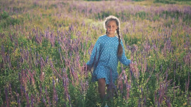 Girl in flower field. Child touches blue flowers with his hand. Girl in blue dress. Child hand touches flowers. Happy little girl outdoors in flower field. Natural beauty. Happy childhood concept