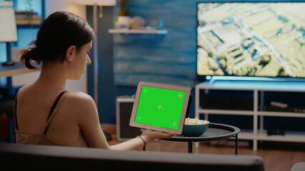 Young person looking at tablet with horizontal green screen background sitting in living room on...