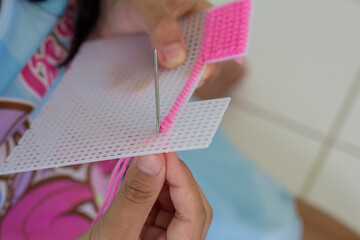 Hand of child holding needle lacing on Plastic mesh canvas or vinyl weave to do invention and is an exercise in meditation.