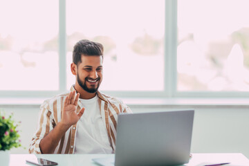 Happy indian man with laptop computer having video chat and waving hand at home office