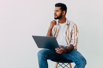 Portrait of business Indian man using laptop computer, looking side and smiling, standing on white...