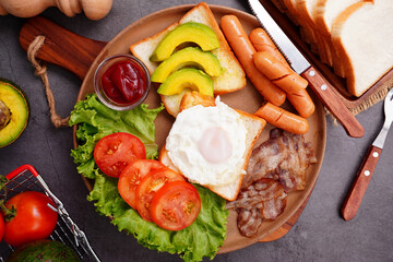 European breakfast toast eggs bacon  ​​sliced ​​tomatoeswith hot dog and vegetables in a round plate.
