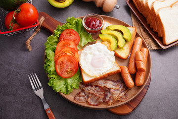 European breakfast toast eggs bacon  ​​sliced ​​tomatoeswith hot dog and vegetables in a round plate.