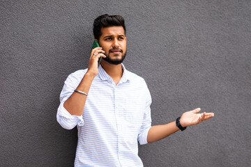 Young man smiling happy talking on the smartphone leaning on the gray wall
