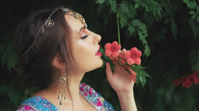 Closeup portrait indian woman. Oriental girl princess enjoy scent aroma blossoming tree. Traditional makeup bright pink eyeshadow cat green eyes. Silver earrings adorn girl, teak tiara on forehead
