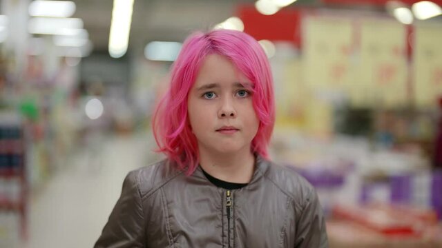 Mysterious look into the camera of a beautiful teen with pink hair standing in a shopping mall
