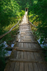 Suspended wooden bridge over a small river in a summer forest