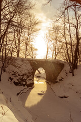 Stone bridge in winter forest at sunset