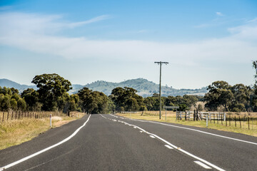 Open empty road surrounded by farms and fields in Australia. Mountains on the horizon. Road trip travel