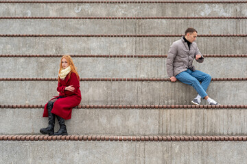 young couple in a quarrel, a guy and a girl are sitting far from each other in the empty stands