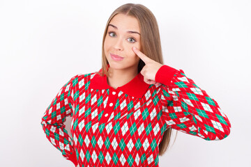 Young caucasian girl wearing christmas sweaters on white background, looking, observing, keeping an...