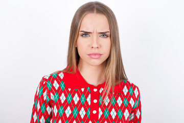 Young caucasian girl wearing christmas sweaters on white background frowning his eyebrows being displeased with something.