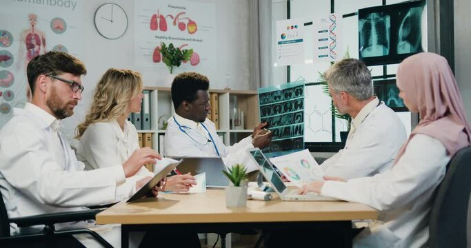 Workflow in hospital where likable confident responsible skilled diverse male and female doctors analyzing results of x-ray image during joint briefing