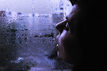 A sad woman blows air with her lips on window fogged from the rain. The concept of autumn...