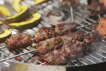 narrow closeup on fresh kofta lamb meat spits and pumpkin slices that are grilled on a charcoal grill - barbecue scenery with selective focus