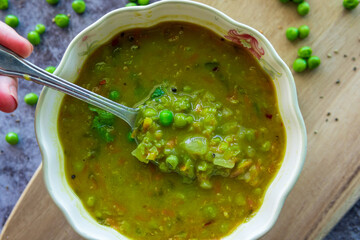 Eating Homemade pea soup with a spoon that is rich in flavors, vegetables, and healthy ingredients. Hot green split pea soup for winter in a decorative bowl served on a wooden board. Fresh and tasty.