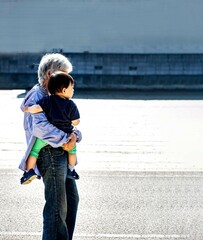 1才の男の子をおばあちゃんが抱っこして道を歩いている　立っている