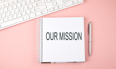 Pink office desk with keyboard and notebook with text OUR MISSION