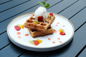 Belgium waffles with fruits and ice cream. Served with plate on wooden table. Selective focus image and close up.
