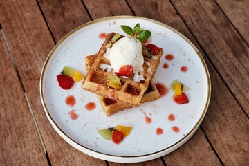 Belgium waffles with fruits and ice cream. Served with plate on wooden table. Selective focus image and close up.
