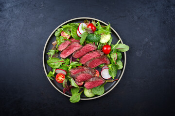 Modern style traditional fried dry aged bison beef rump steak slices with vegetable, lettuce and parmesan cheese served as top view in a Nordic design plate with copy space