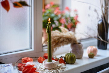 autumn still life on the windowsill on the eve of Halloween, a burning candle, pumpkins and dry herbs, the atmosphere of autumn comfort with candles.