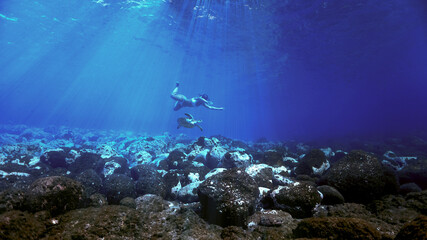 Fototapeta na wymiar Girl swimming with turtle in rays of light underwater
