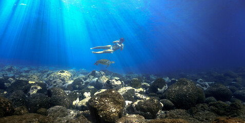 Snorkeling girl swimming with turtle in rays of light underwater