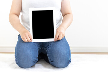 カーペットに座って、タブレット端末を使う女性のイメージ（30代、日本人、顔無し）