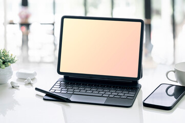blank screen tablet with magic keyboard and smartphone on white table in office room.