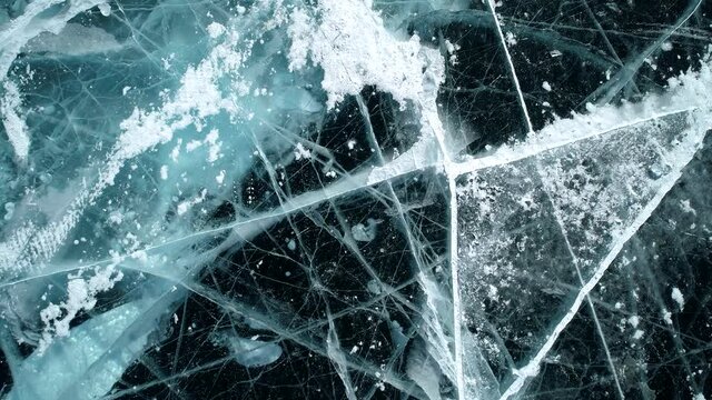 Aerial above the blue transparent clear ice with cracks and bubbles inside. Frozen Lake Baikal. Natural landmark. Winter landscape. Popular touristic destination. Top down view.