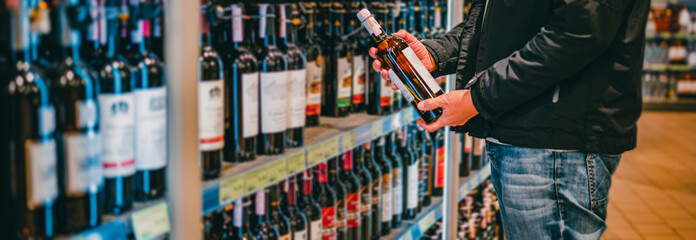 man hand holding bottle wine in grocery store in supermarket