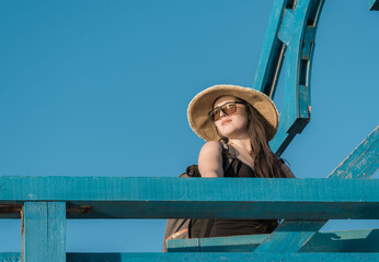 Girl tourist in sunglasses and a hat with a backpack on a wooden pier