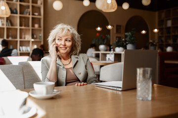 an adult attractive experienced blonde woman talks on a mobile phone, calls to a business partner on work issues, the interior of a cafe