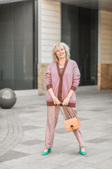 Attractive adult blonde of European appearance in a pantsuit with a handbag in her hands on the streets of the city