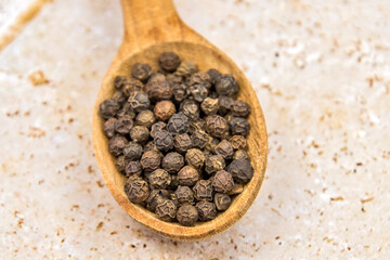 poivre en grains dans une cuillère en bois en gros plan sur une table