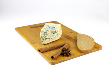 A piece of blue cheese, a slice of rye bread, cinnamon sticks, and anise star on a wooden board. Isolated on white.